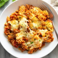Lazy Lasagna in a white bowl with melted mozzarella cheese and parsley on top and a fork on the side.